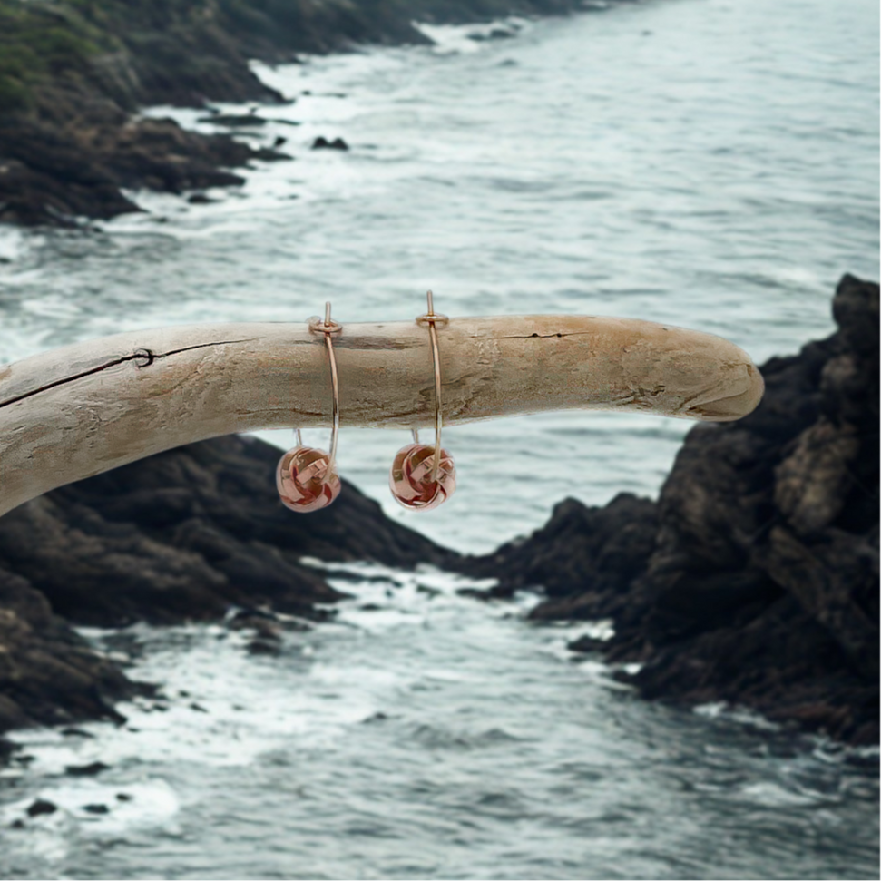 Rose gold earrings hanging from a piece of driftwood with a coastal background